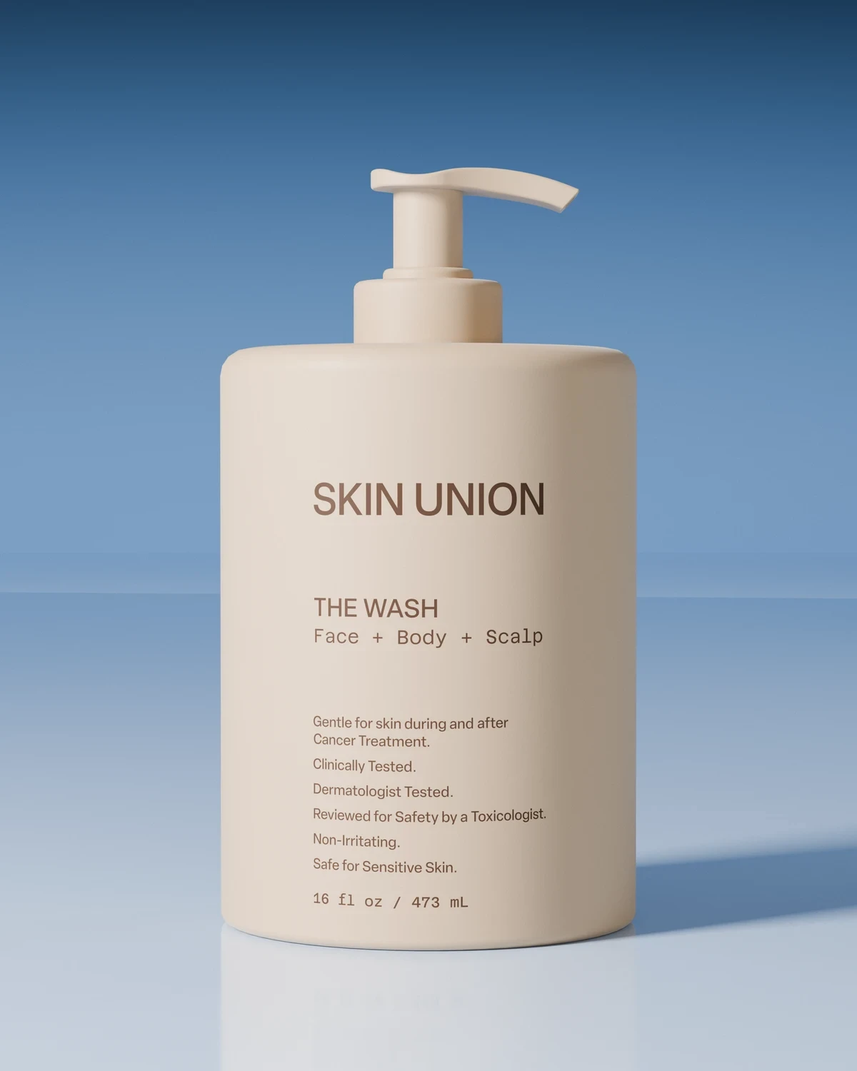 The Wash — a pale pump bottle labelled Face + Body + Scalp, on a soft white surface against a blue backdrop